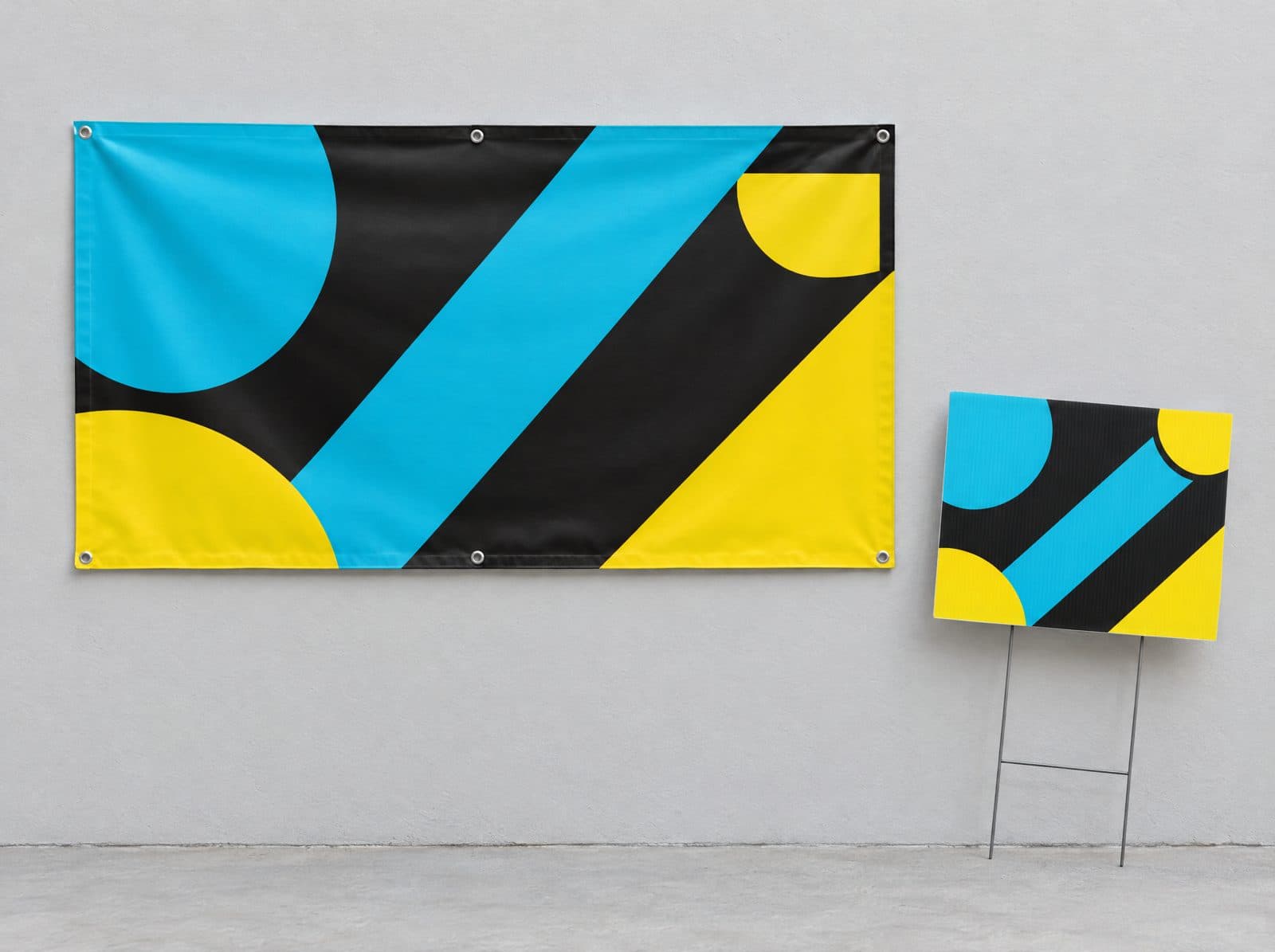 A vinyl banner with grommets on a wall beside a coroplast yard sign on a stake